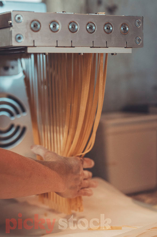 Chef uses hands to pull fresh pasta from pasta machine. 