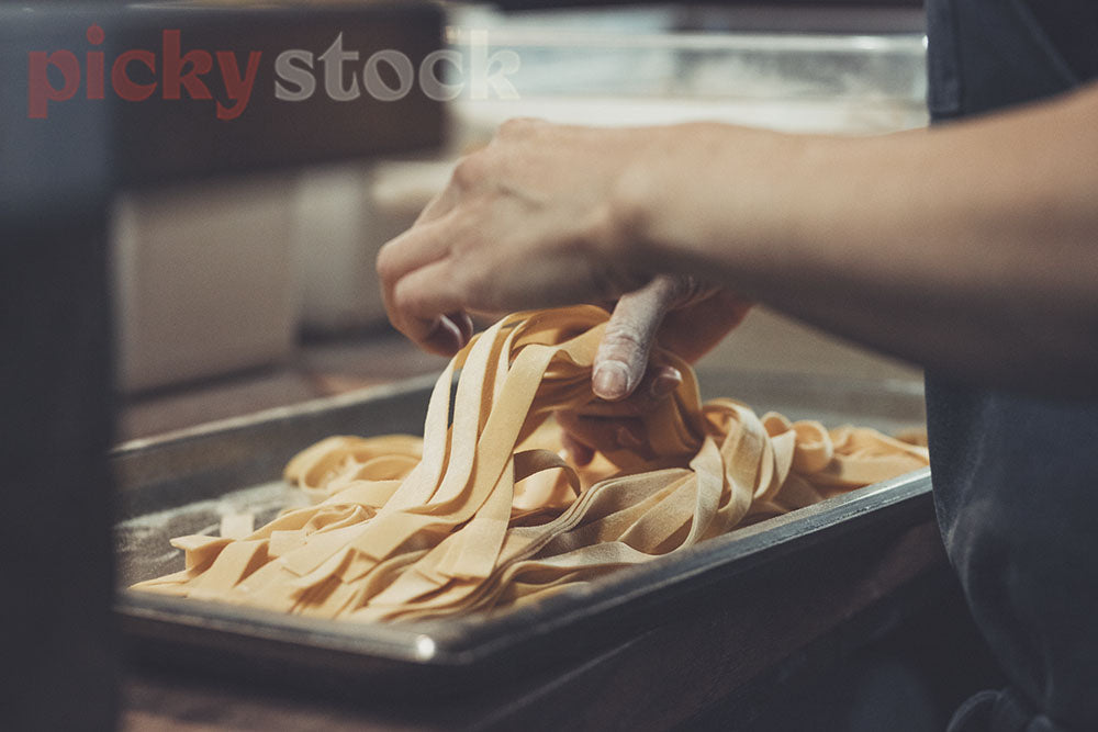 Hands pick up fresh pasta from tray, ready to cook.