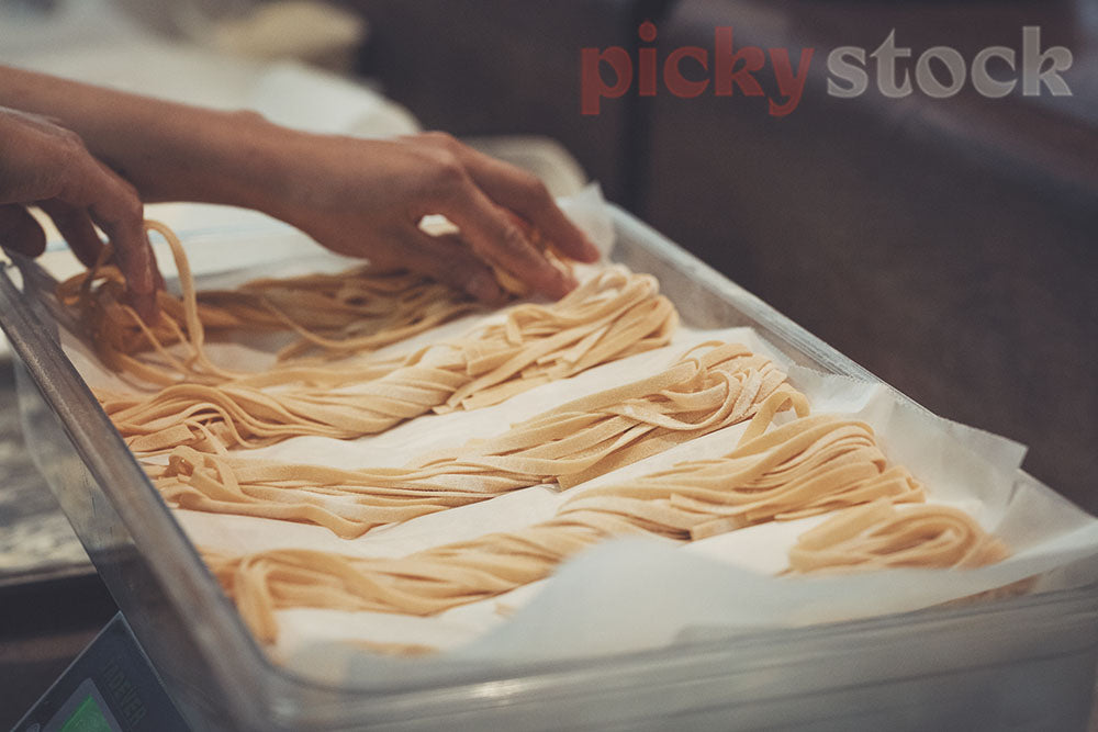 Hands lay out freshly made pasta on tray. 