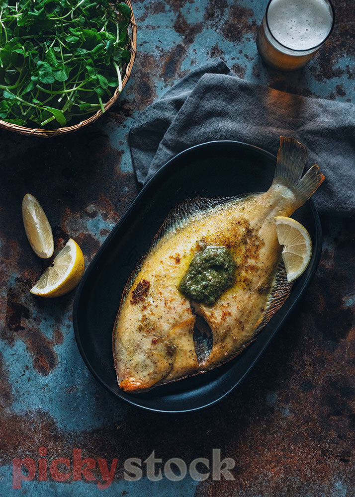 Stylish image of flounder with watercress and beer, on dark plate on dark table. 