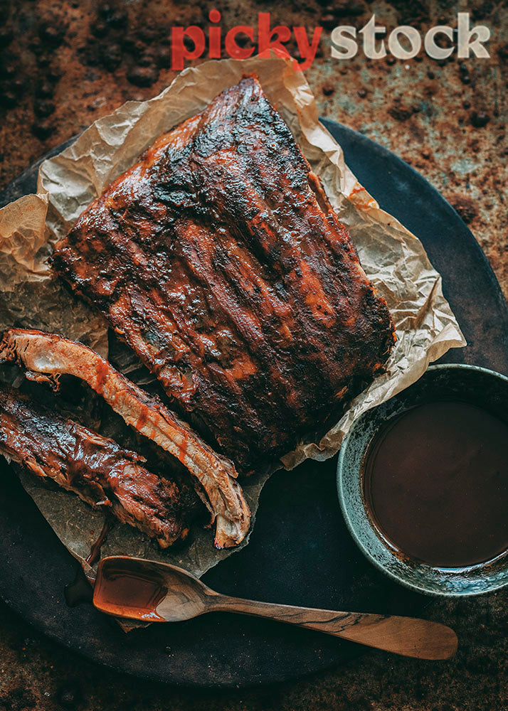 Barbecue Ribs with glaze sitting on cooked baking paper, on rustic table setting. 
