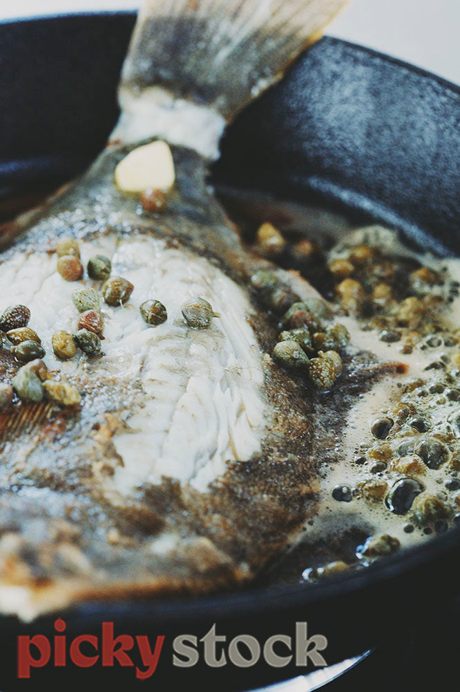 whole flounder being panfried with butter and capers 