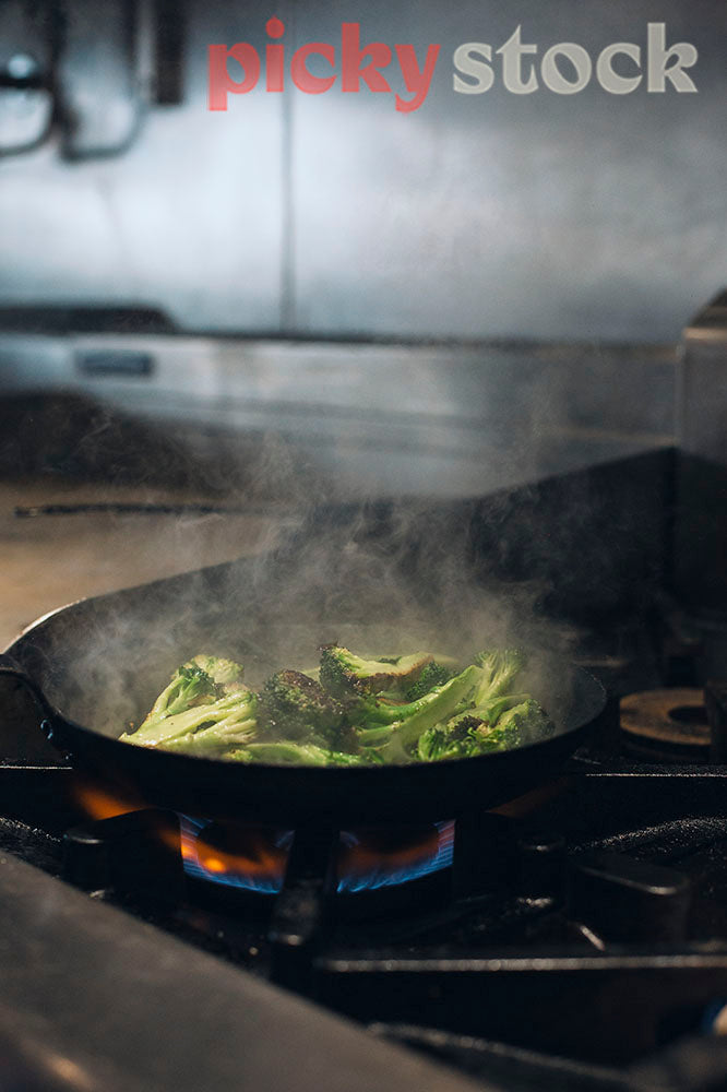 panfrying broccoli on a restaurant stovetop, steam coming out