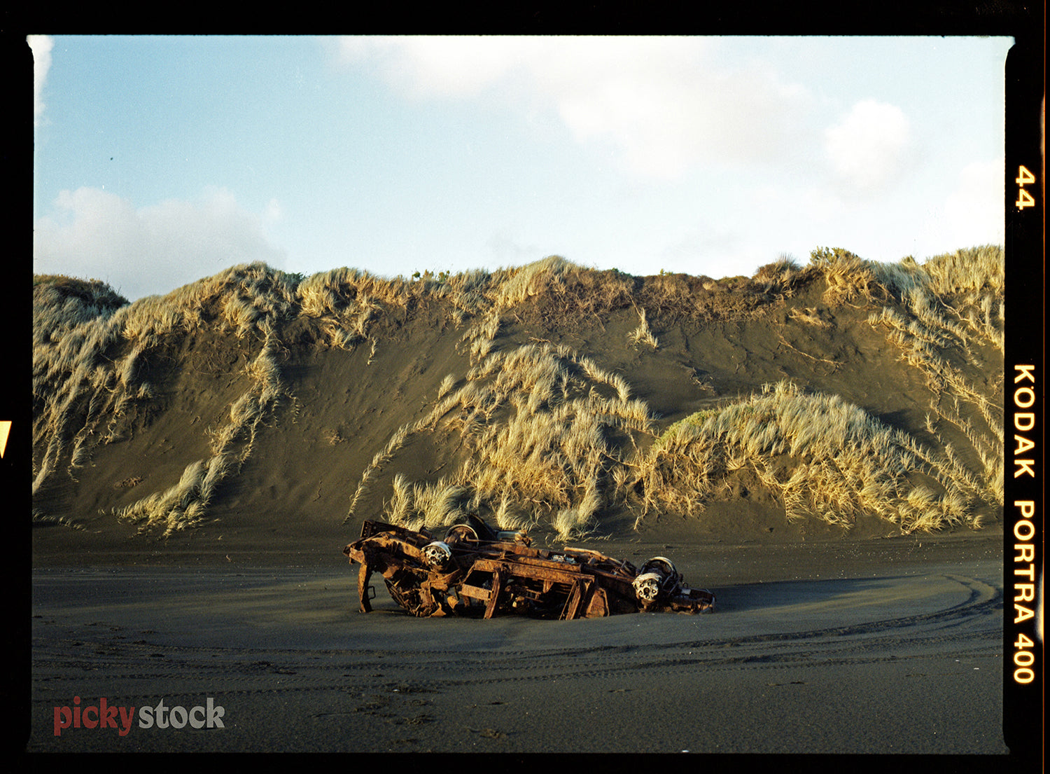 Rusty car wreck on black sand beach cooking back towards sand dunes. 