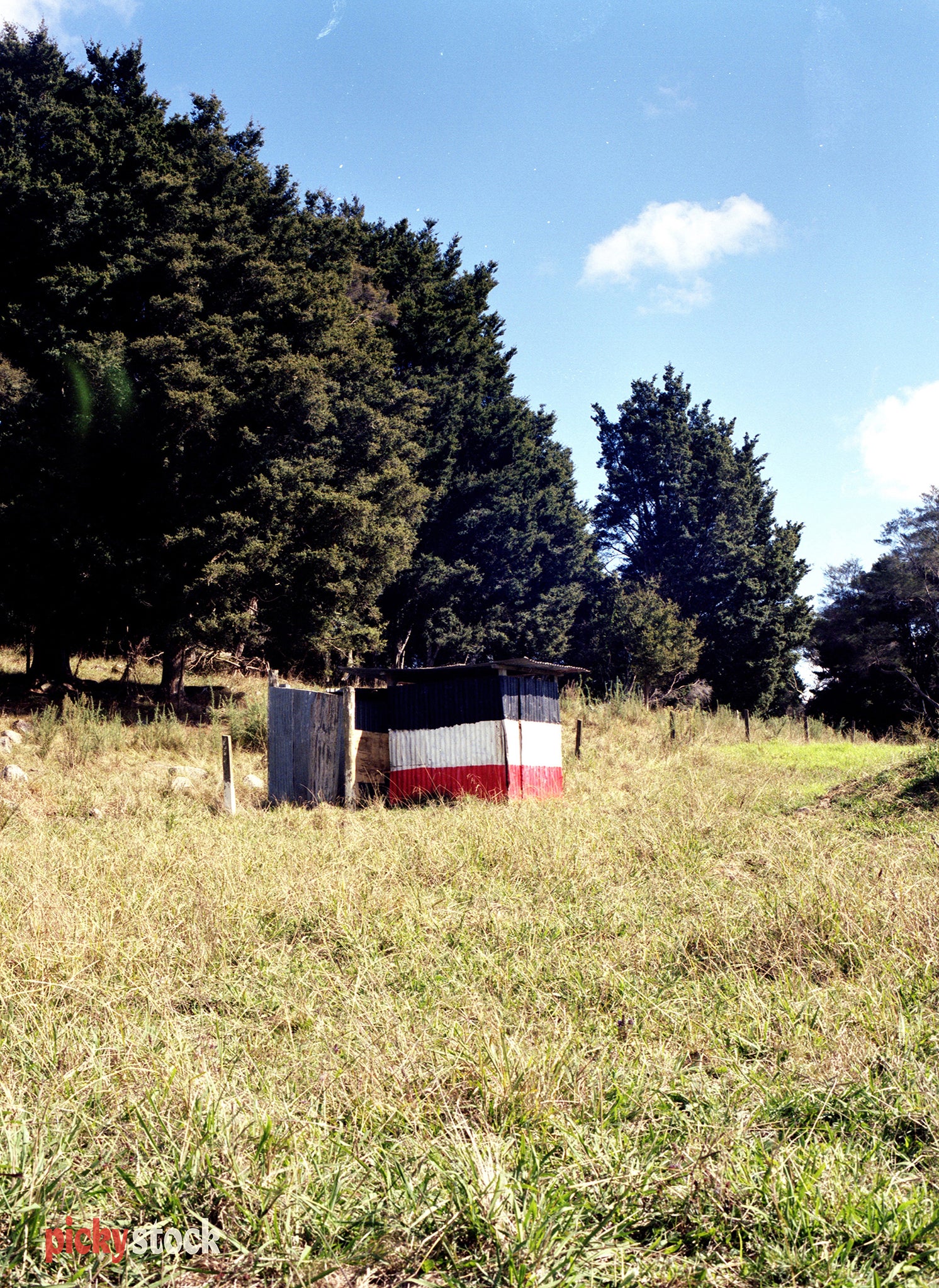 Colourful red, white and navy tin shed against the hills.