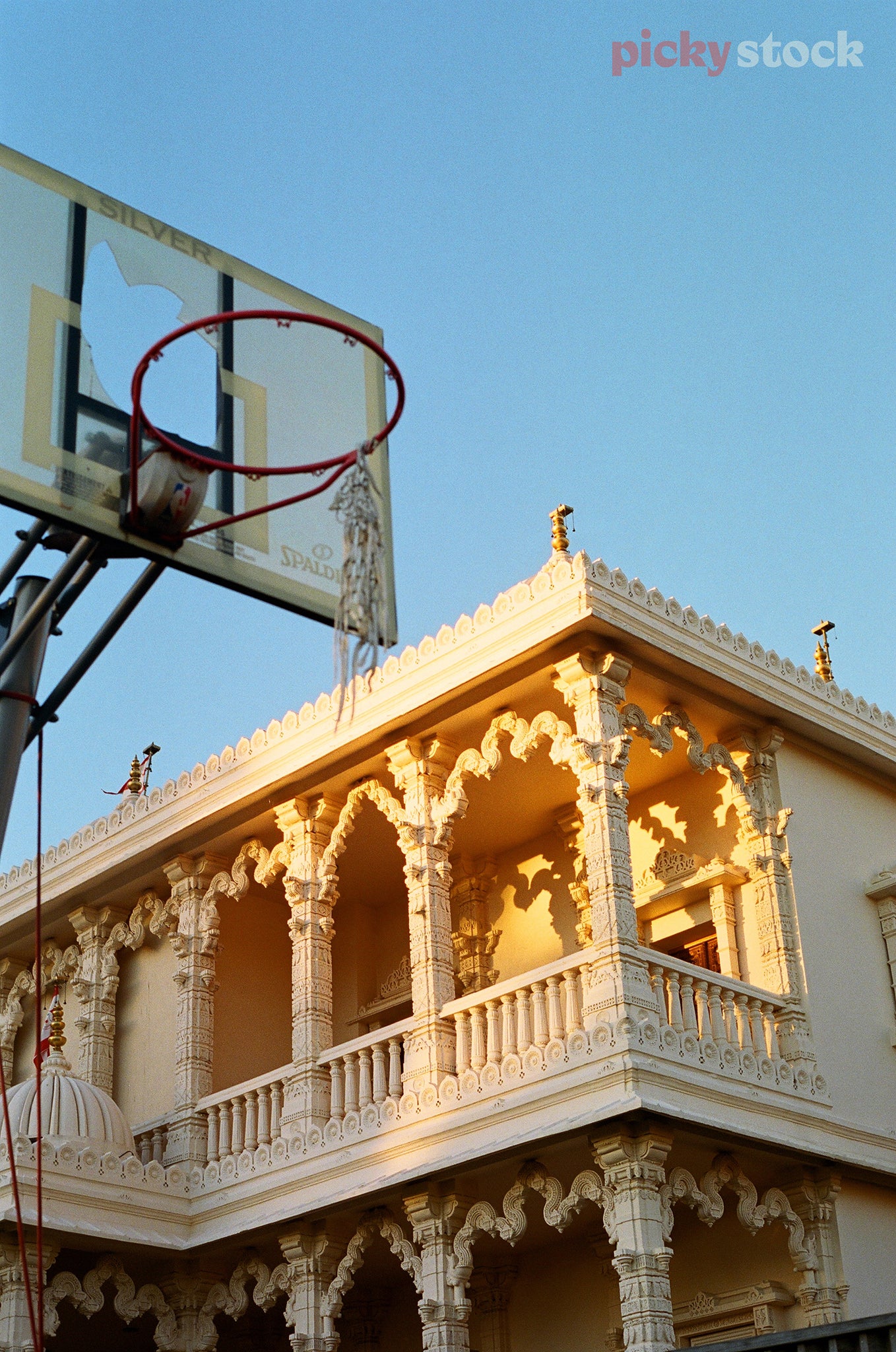 Basketball hoop with netting falling off it, sits against a cultural centre. 