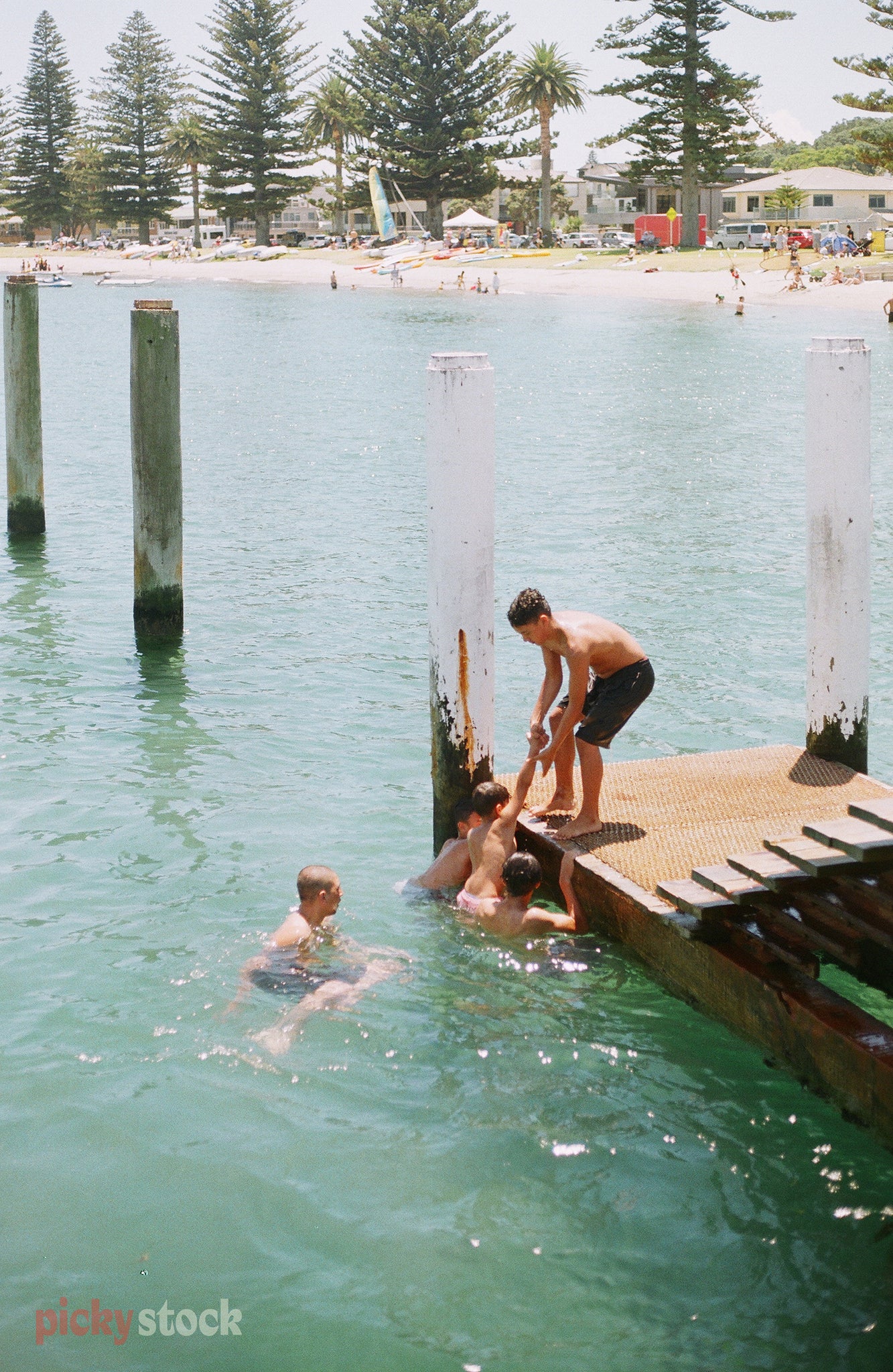 Children help each other up out of the water towards the jetty in mid summer.