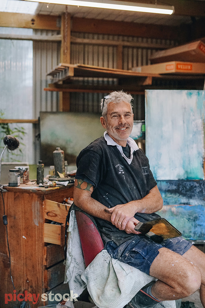 Painter sitting in his art studio surrounded by his artwork 