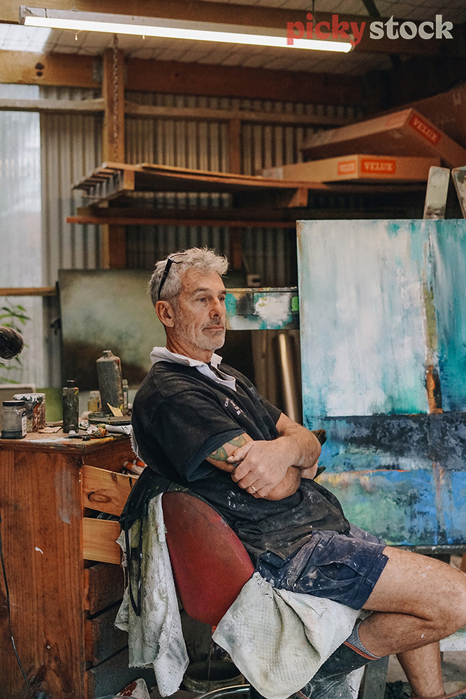 Painter sitting in his art studio surrounded by his artwork 