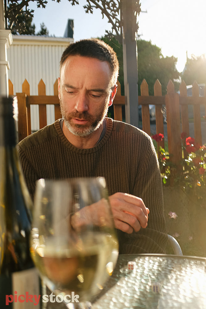 Man sitting in the sun outside his house with a glass of wine