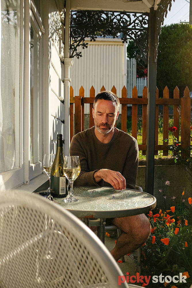 Man sitting in the sun outside his house with a glass of wine.