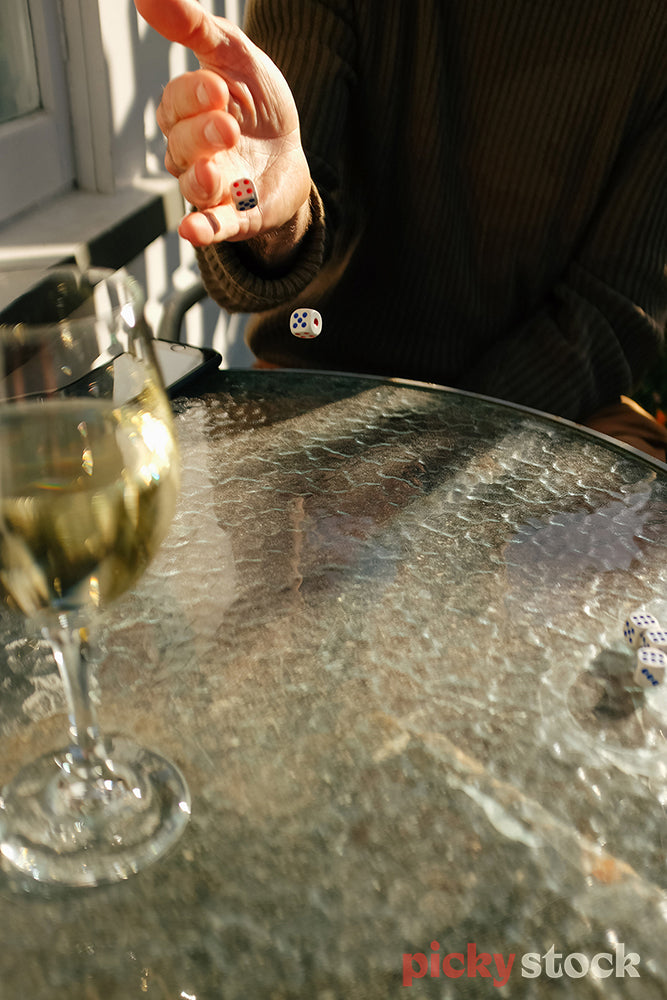 Close up of hand throwing dice next to a glass of wine in the sun