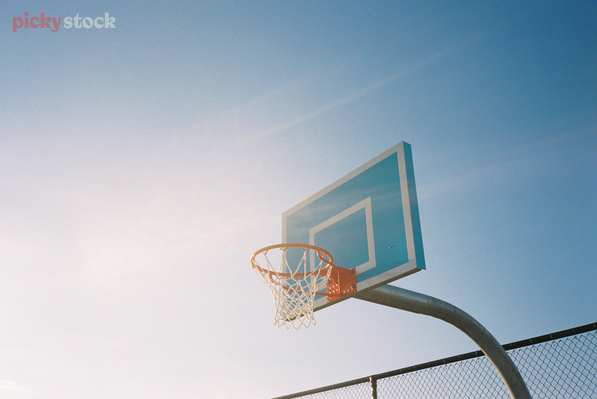 Looking upwards towards a blue basketball hoop on a bright blue day. 