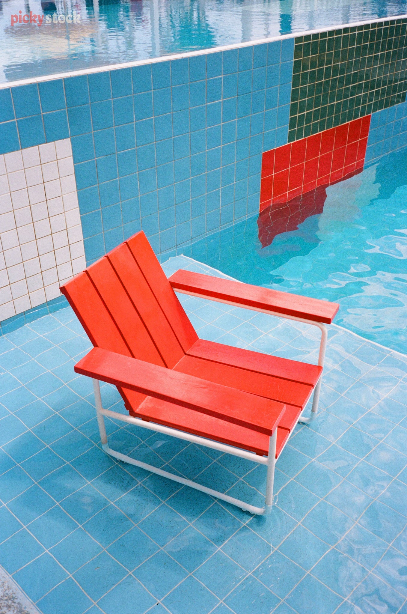 Bright red retro wooden chair sits surmerged in a blue-tiled modernist designed pool.