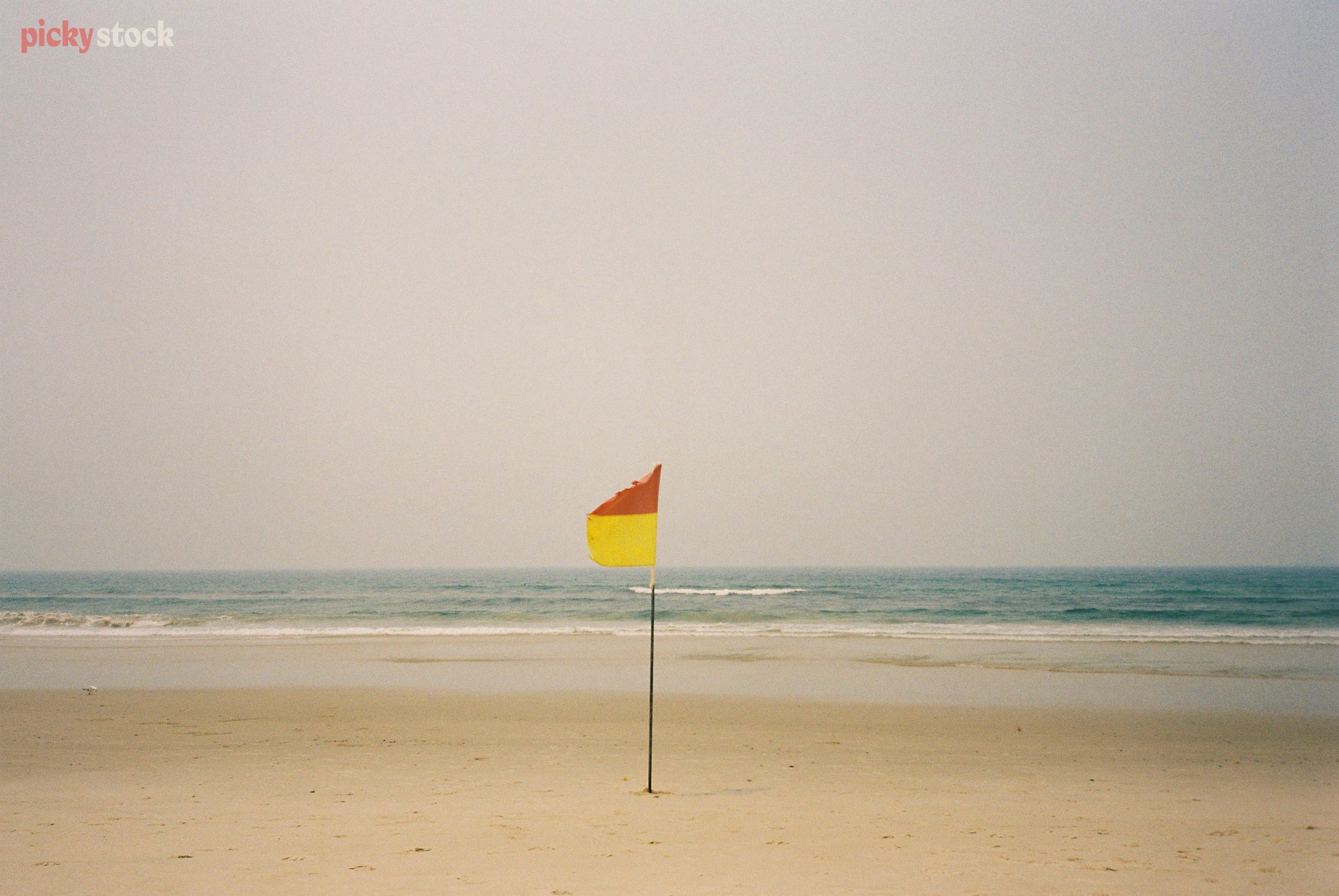 Graphic layout of yellow and red surf flag on a beach. Sand, sea and sky make a graphic style layout. 