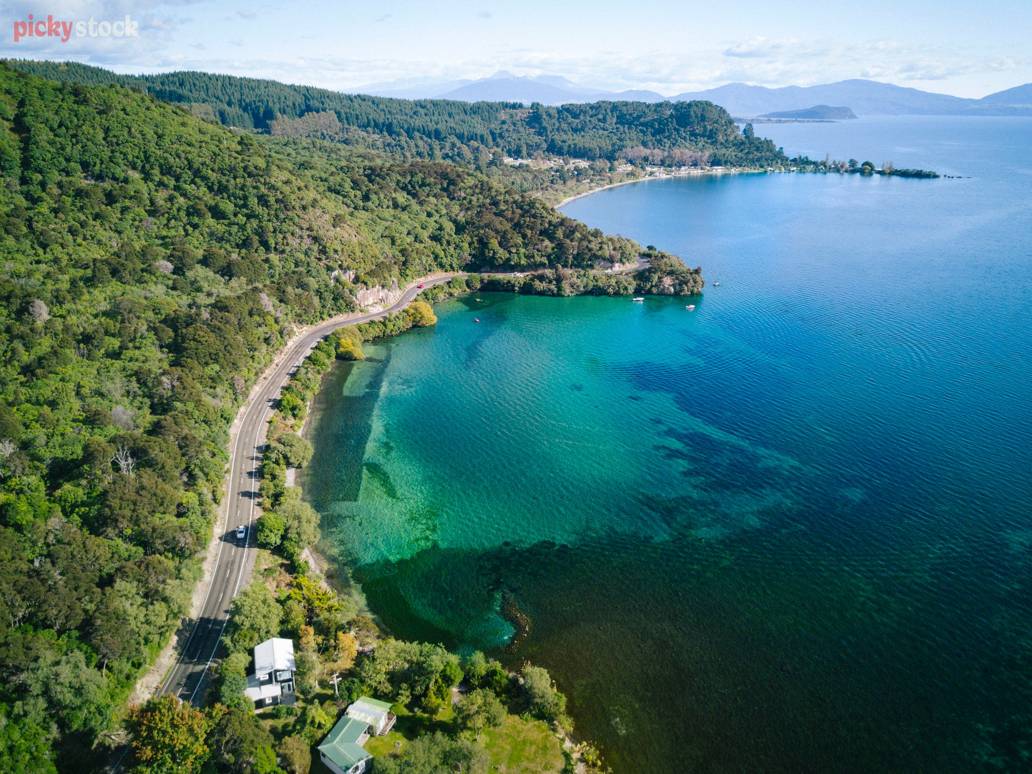Aerial high angle shot of the edge of Lake Taupō. The hills to the left, the road and then the crystal clear still water. 