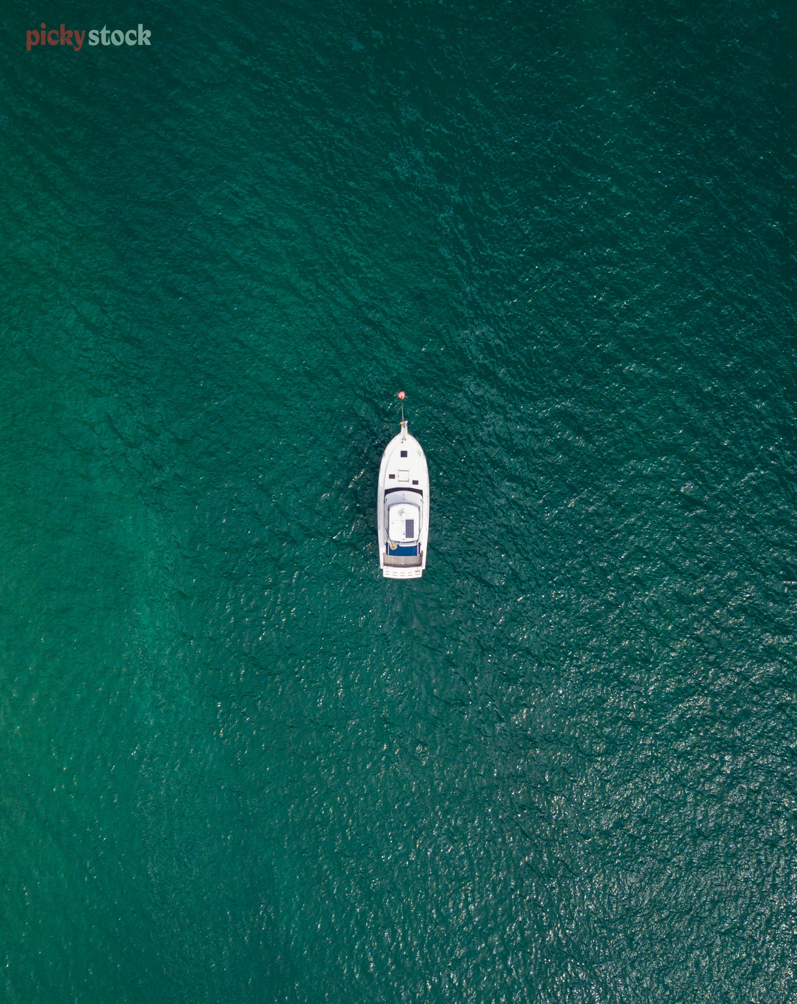 Birds eye image of a lone boat in the middle of the teal coloured still sea. 