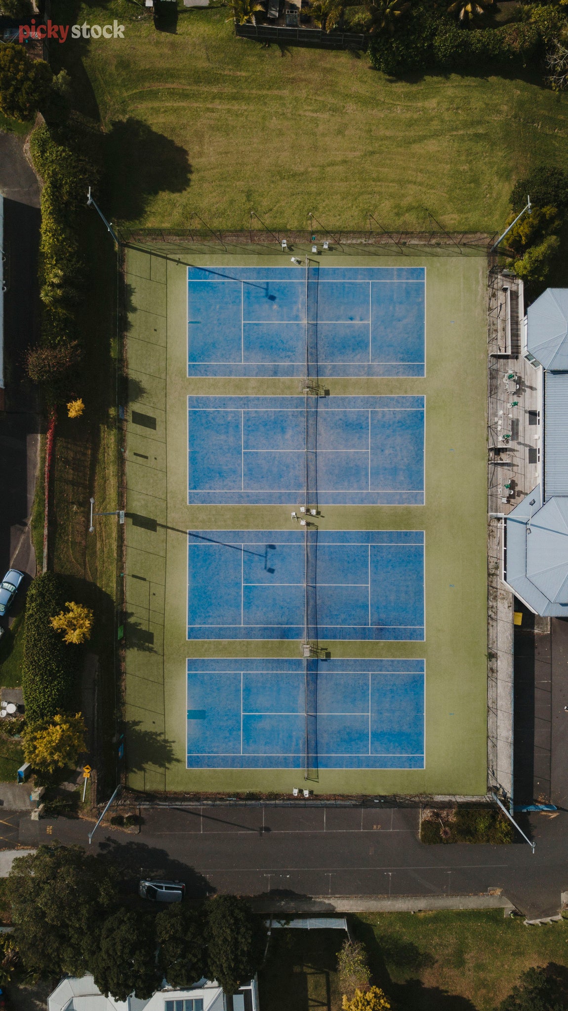 Aerial image of four blue empty tennis courts, surrounded by green grass. 