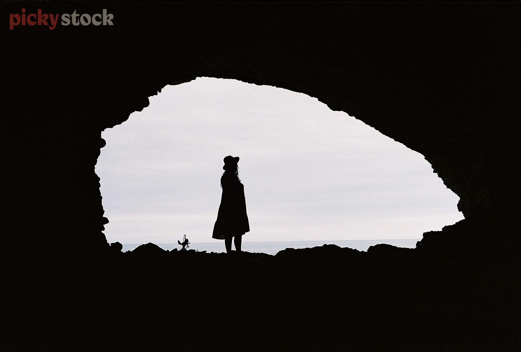 Silhouette of lady standing in the mouth of a cave, the viewier is inside the cave looking out towards the light. 