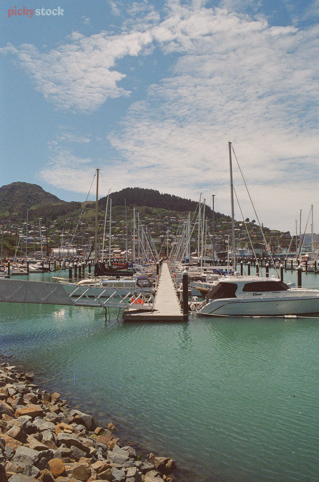 Looking down a marina jetty, lined with sail boats and launches on a bright blue day. 