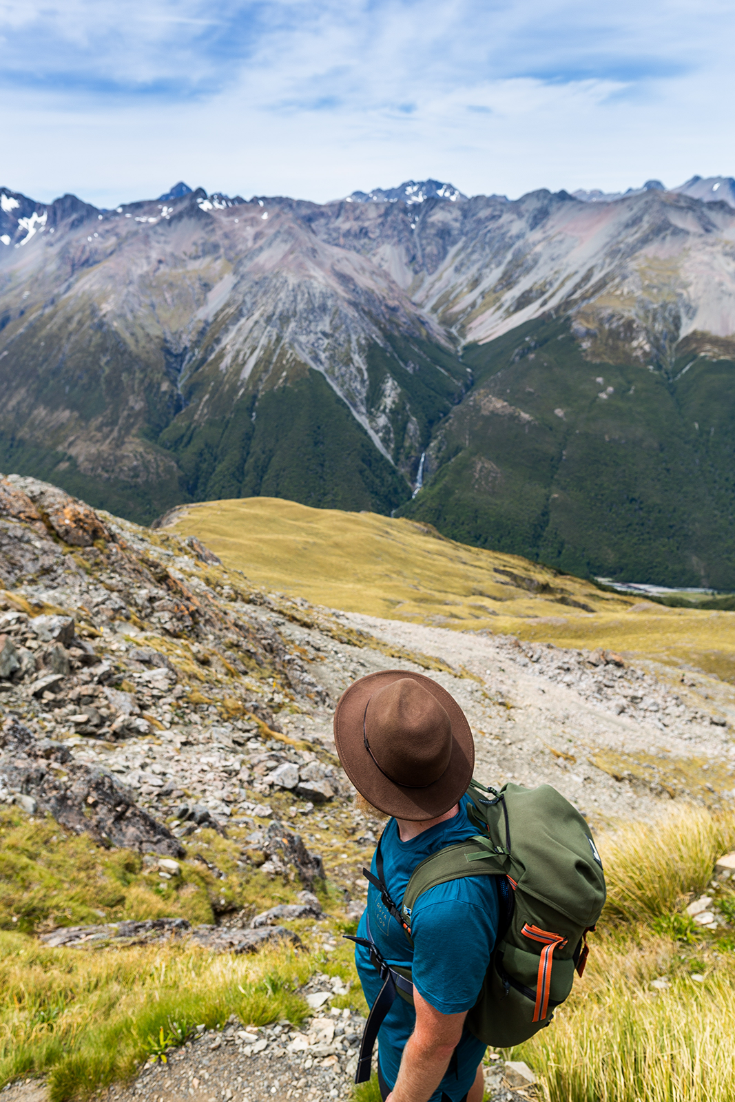 Man hiking mountains stops to take in the view. Wearing a hat he looks out over the valley and mountain range. 