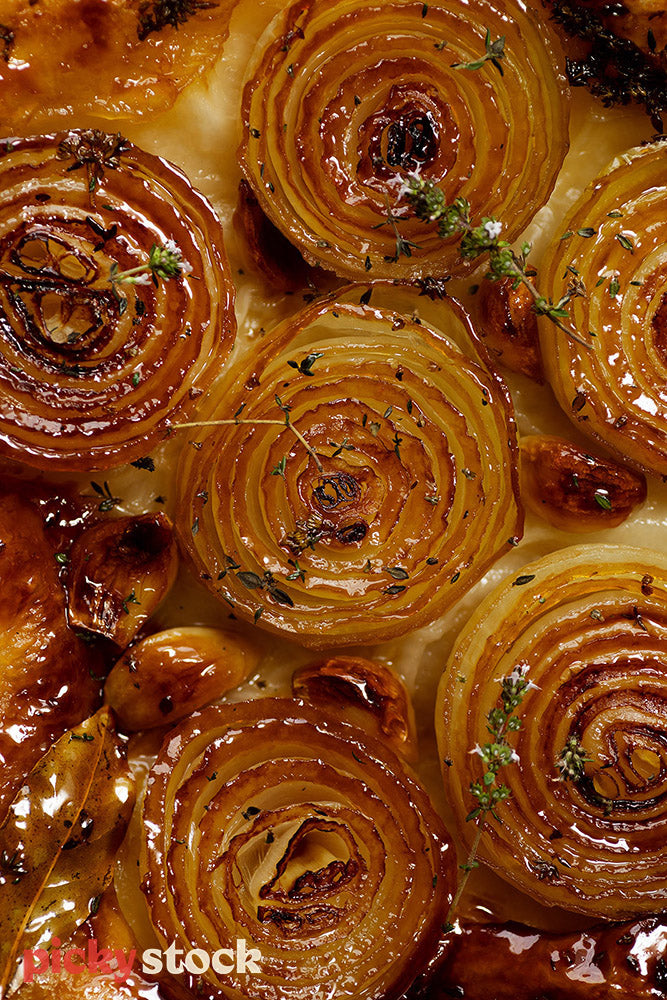 Visual shot of layers of roasted onions with loose gloves of garlic scattered. 