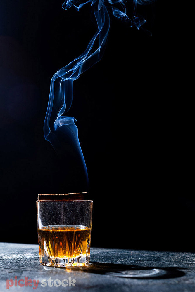 Brown liquor in crystal glass with blue smoke rising from glass. 