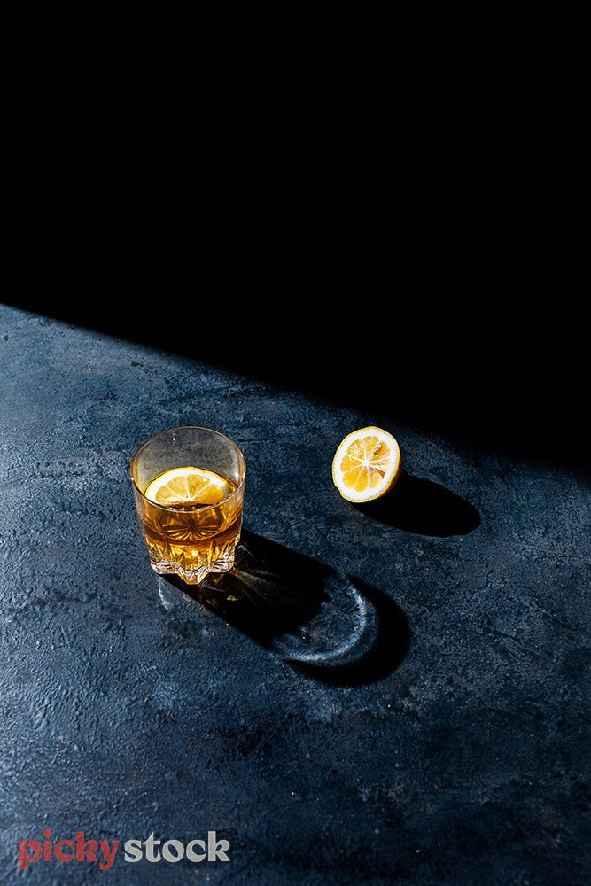 Brown liquor in crystal glass against dark marble surface with slice of lemon.
