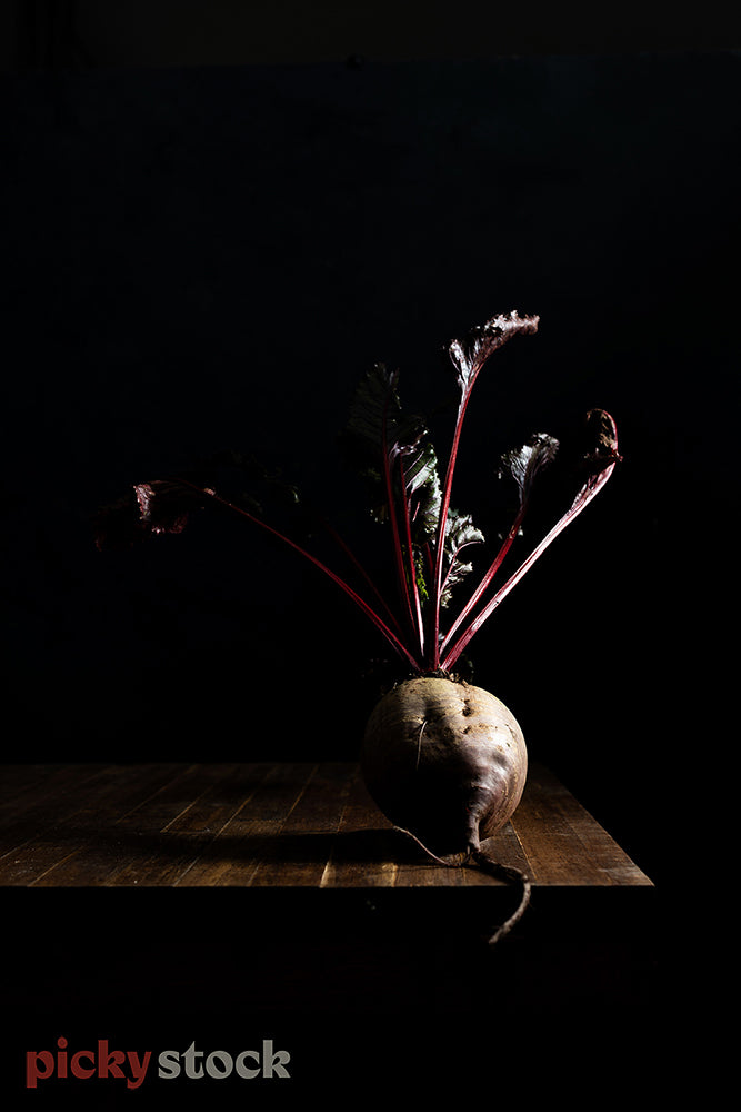 Freshly picked beetroot with roots visible sitting on dark surface.