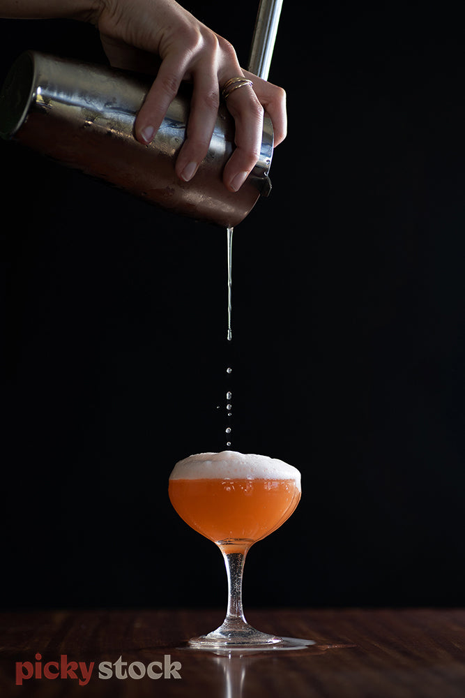 Cocktail being poured from a height from silver cocktail shaker. Female hand 