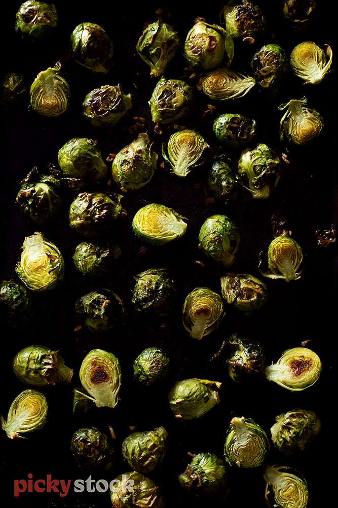 Bunch of cooked caramelized brussel sprouts against dark surface. 