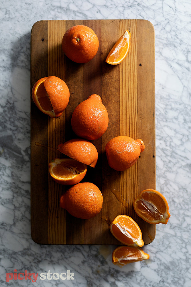 Cut up oranges sitting on wooden chopping board, on top of granite benchtop. 