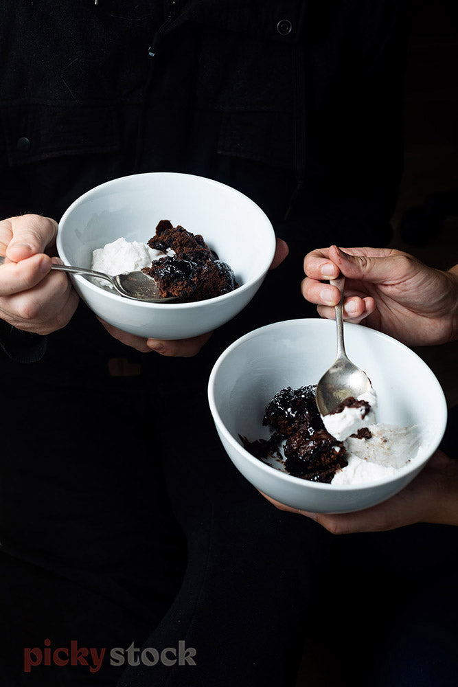 Two white bowls of Chocolate Self Saucing Pudding with Coconut Cream. Hands holding spoon