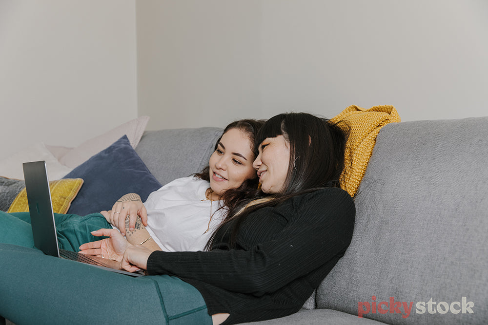 Two female friends chilling on couch looking at laptop screen