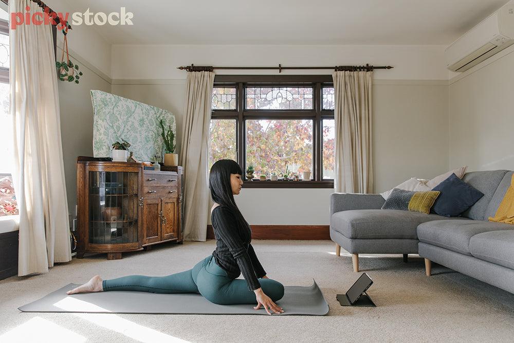 Woman practicing yoga on mat from lounge following along on tablet 