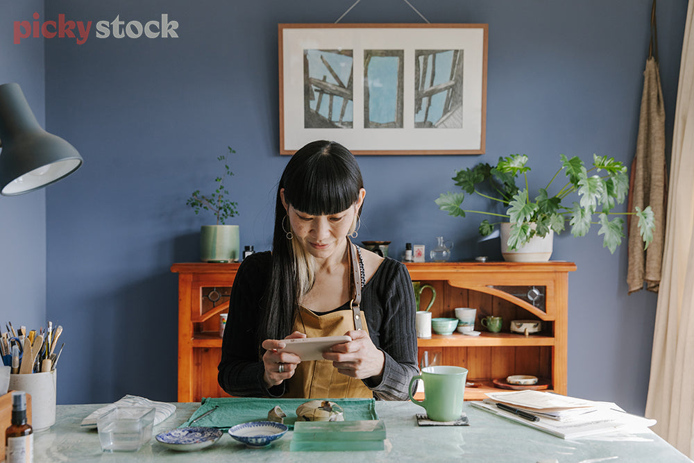 Woman repairing broken ceramic (Kintsugi), while using mobile