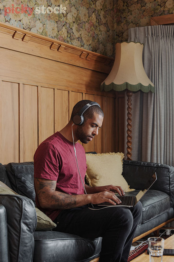 Man on working video call from comfort of couch. Wearing headphones and red top in kiwi living room