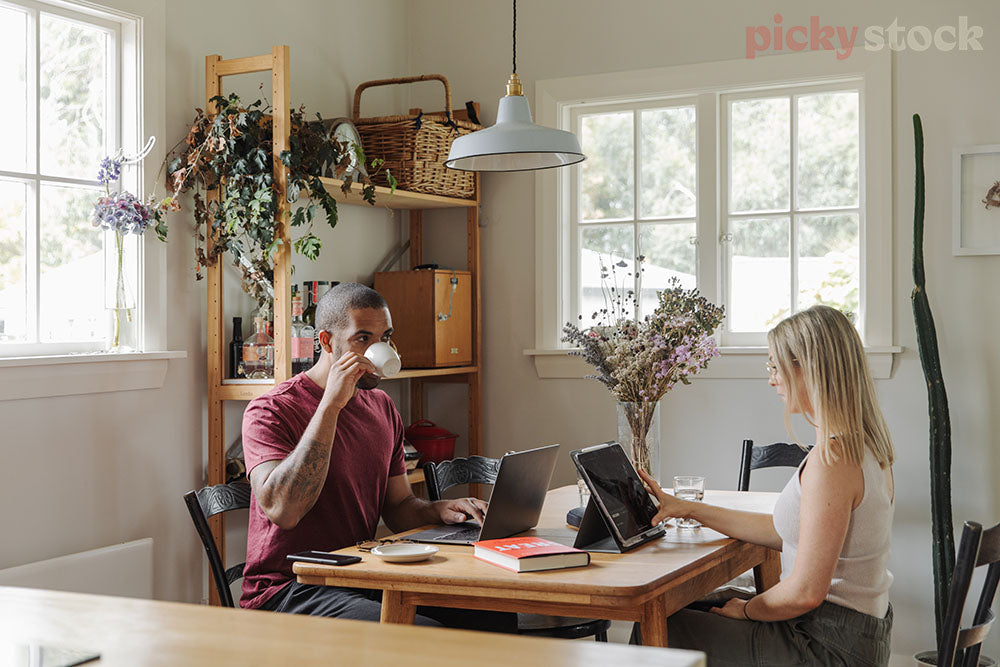 Remote work set up on dining room table.  Man holding white cup and girl wearing clear glass frames