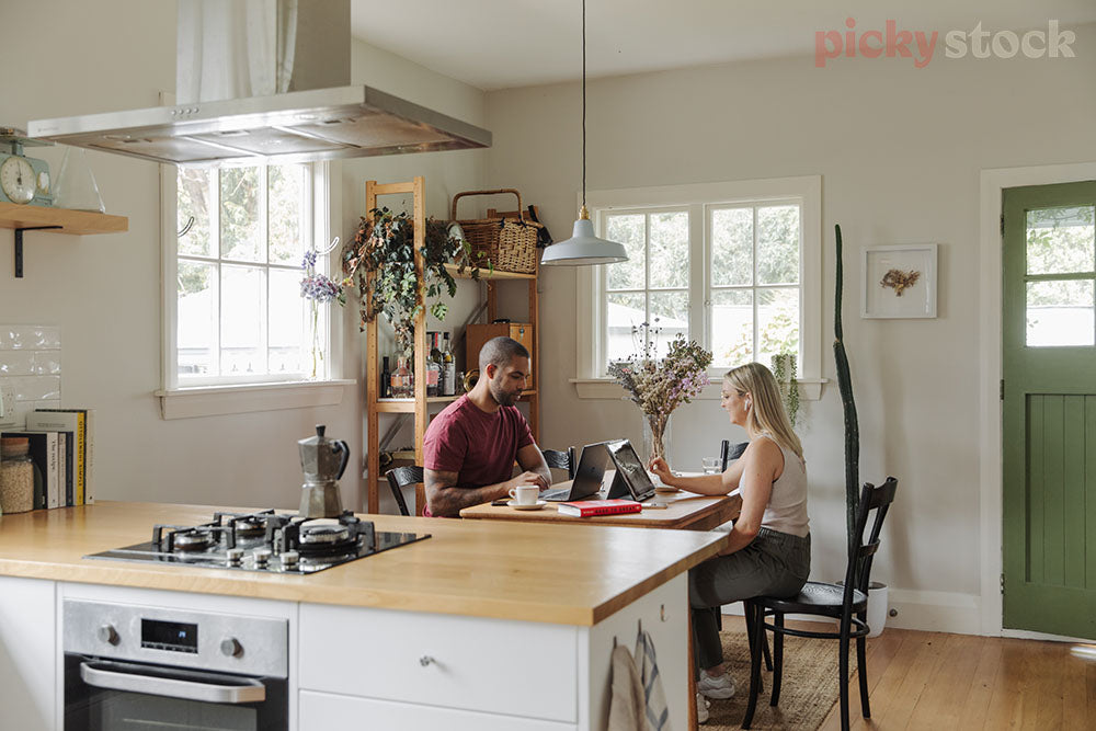 Lady and man sitting around bench in kitchen. Remote work set up on dining room table.  