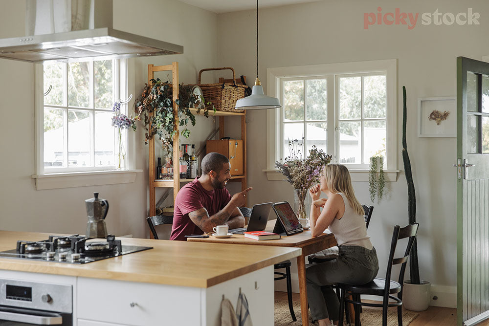 Man and woman working from dining room table, can see kitchen bench in the foreground. 