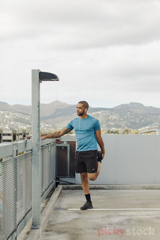 Man wearing headphones stretching before starting workout Wearing bright blue top 