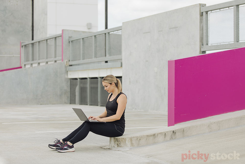 Lady looking at laptop in concrete carpark 