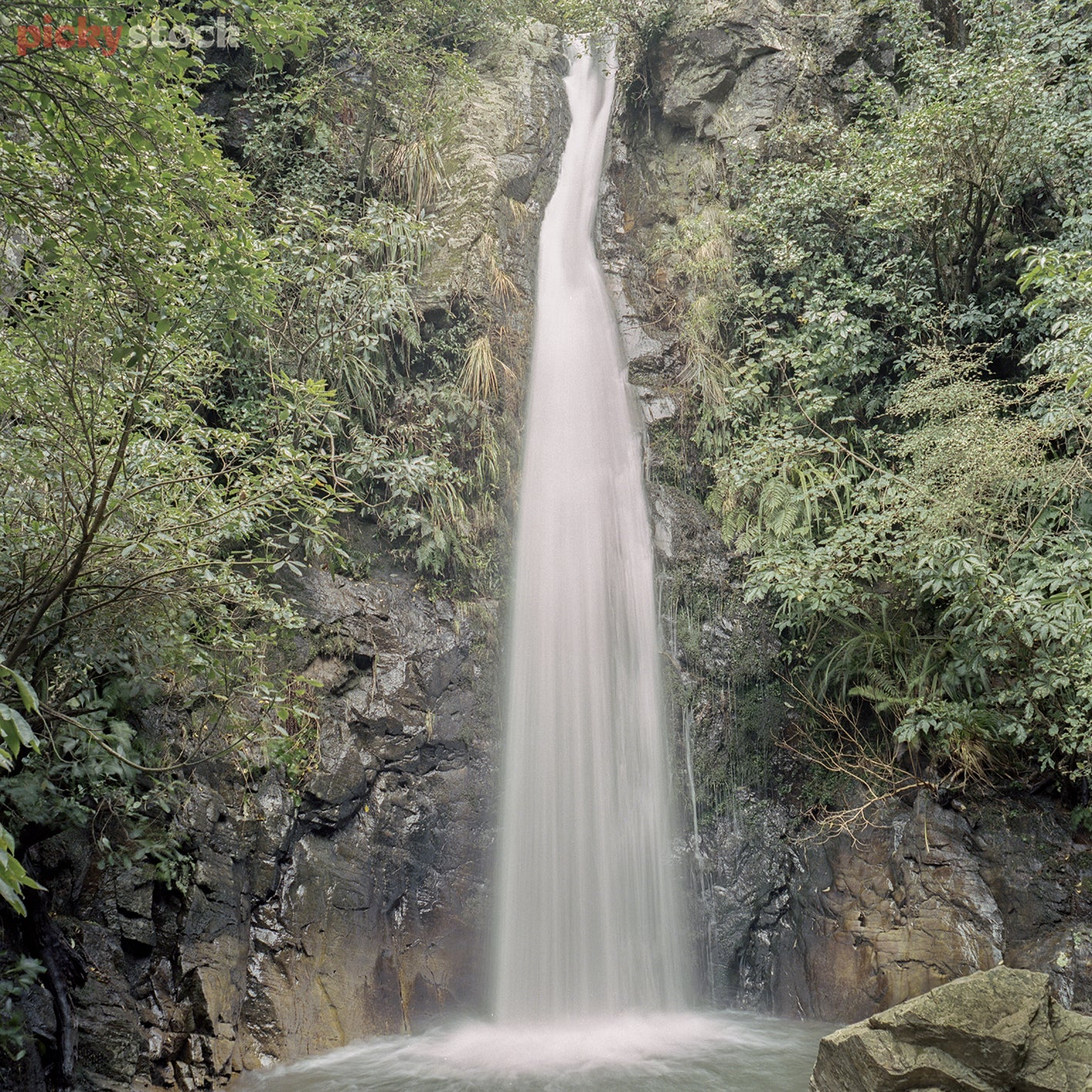 Portrait image of Waspen Waterfall. Large volume of water falling directly in the middle of the image dropping from the top of frame. Bush and greenery 