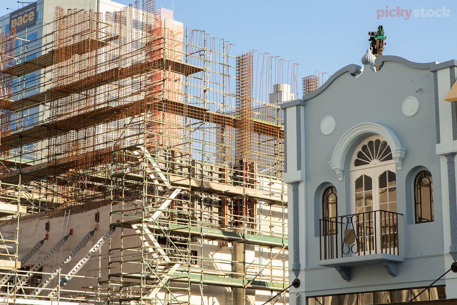 Scafolding and construction surrounding a building after the Christchurch earthquake. Blue sky. Old blue with white trim victorian building left of frame. 