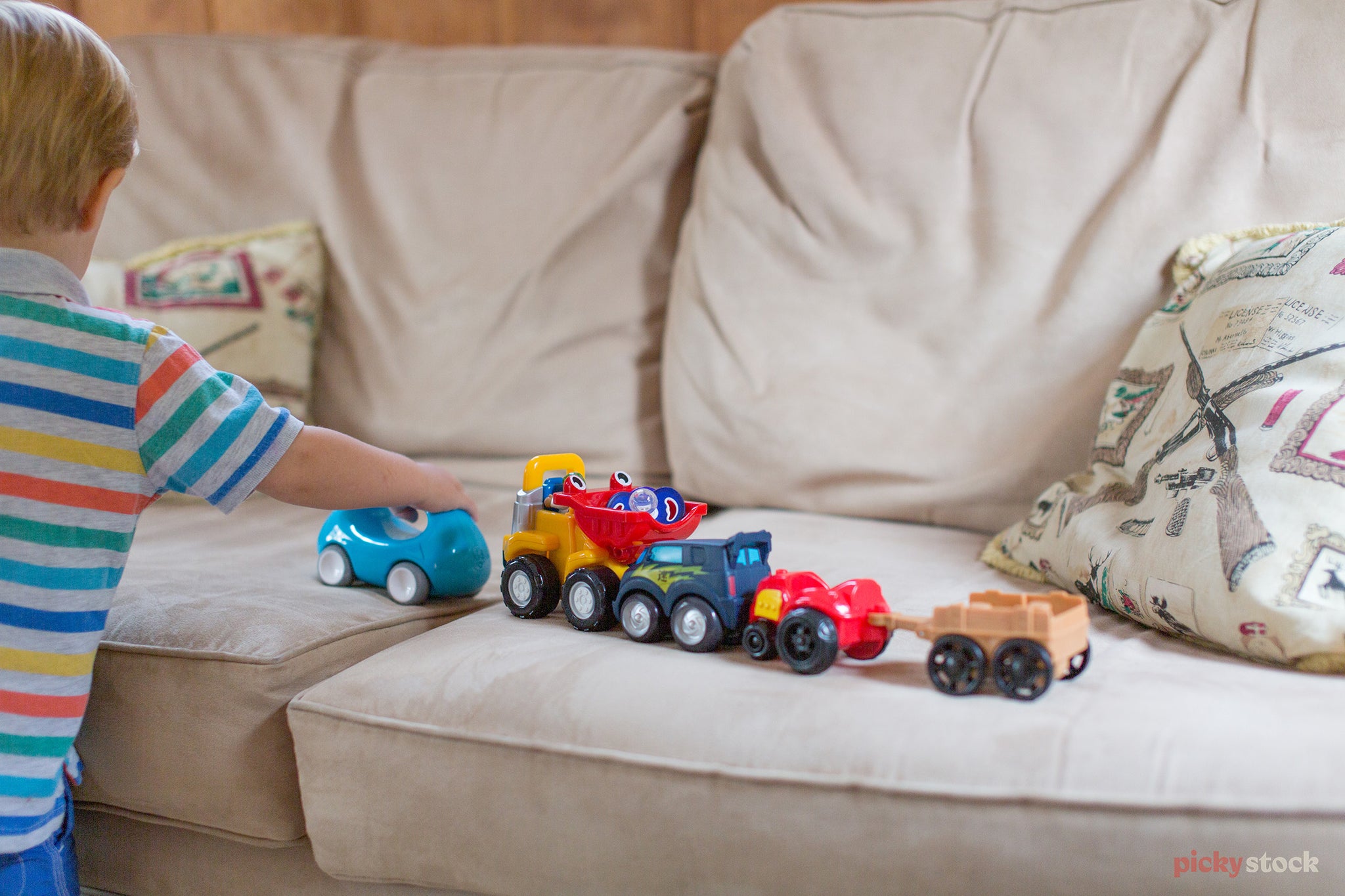 Over the shoulder shot of a child playing with toys, train and truck set along a white couch. 

