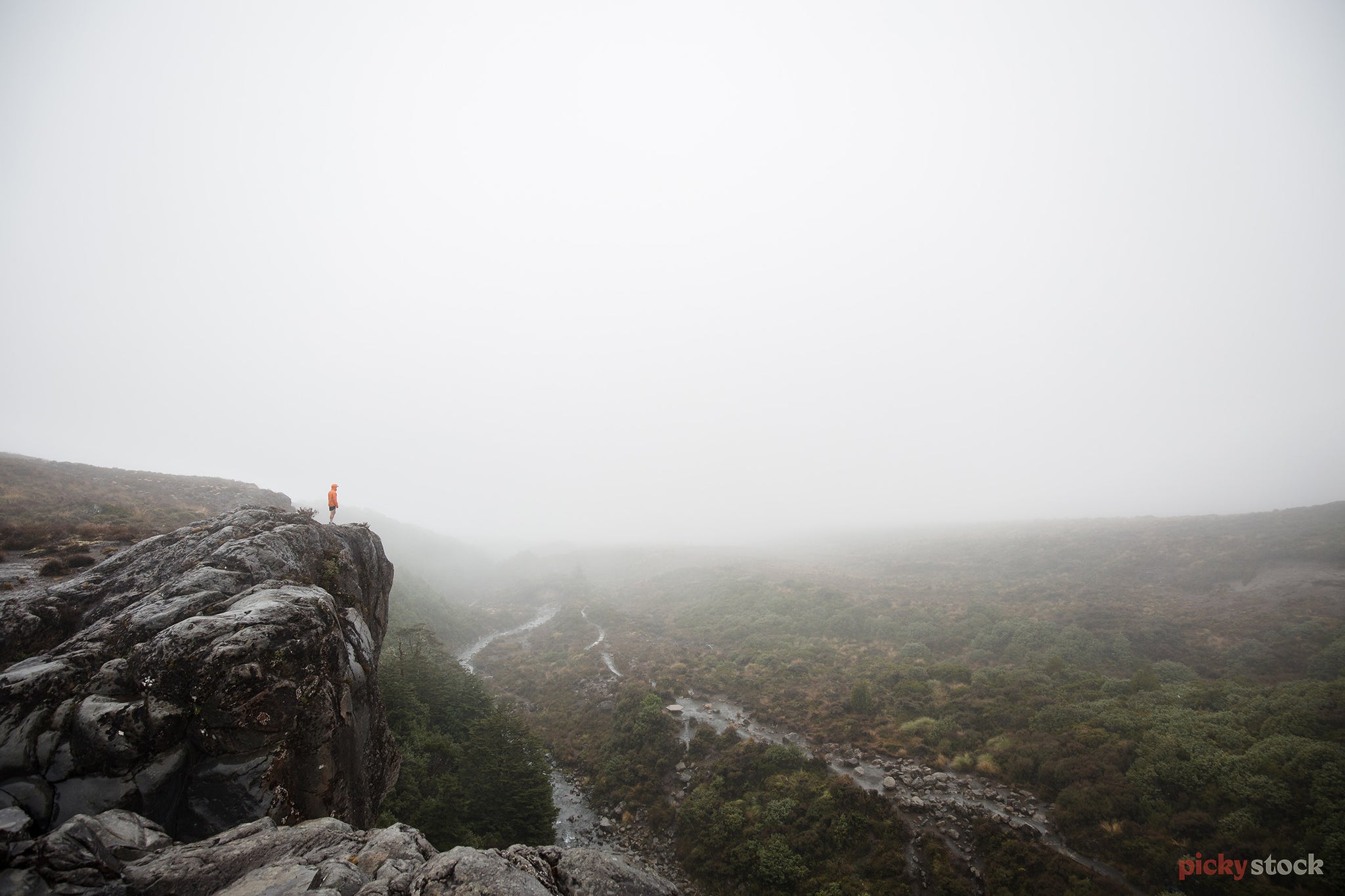 Walker looks out on peak over misty grey gully in the Tongariro National Park region. 