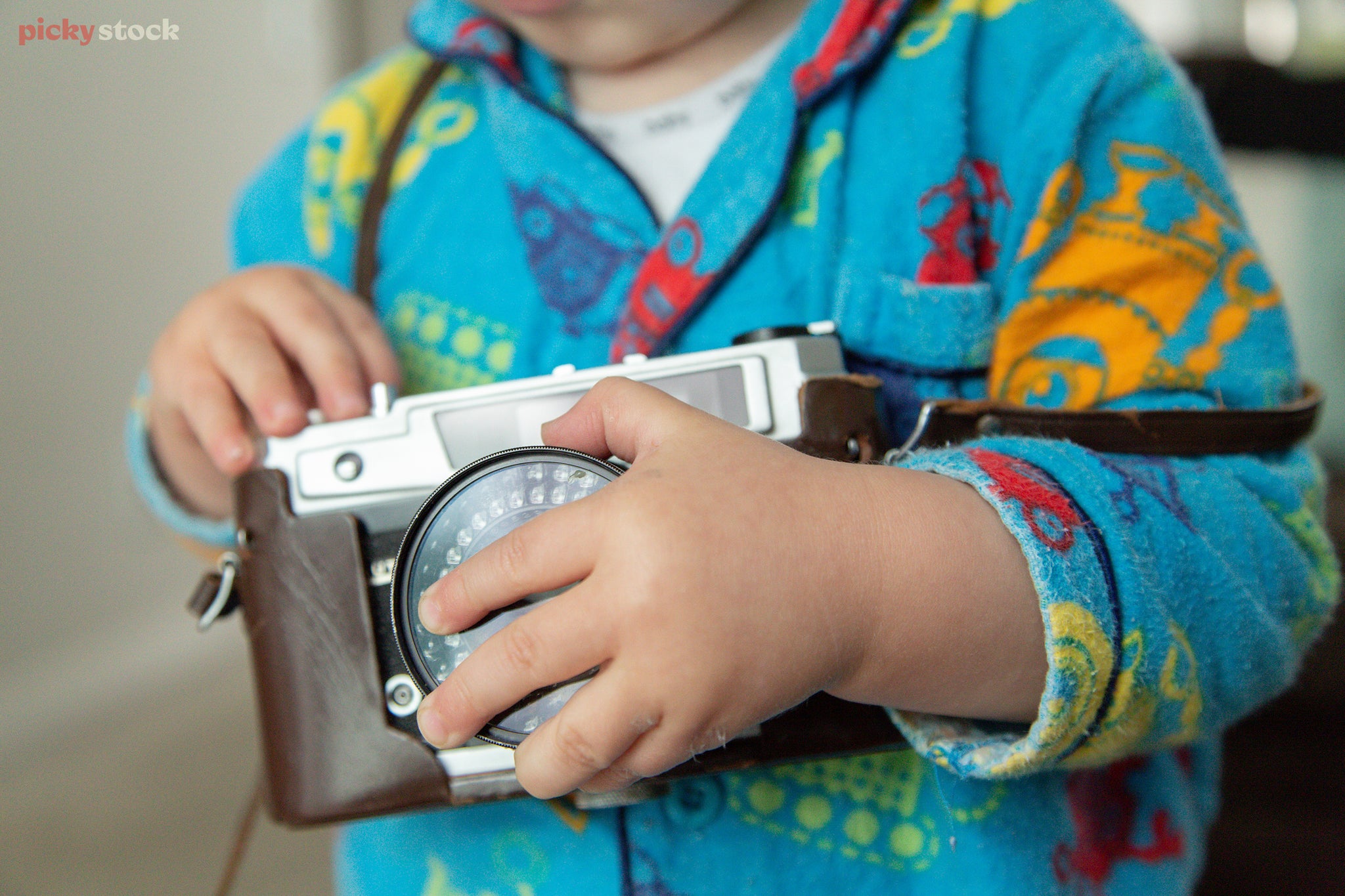 Landscape close up of an infant in pajamas holding a mechanical camera in a leather holster.
