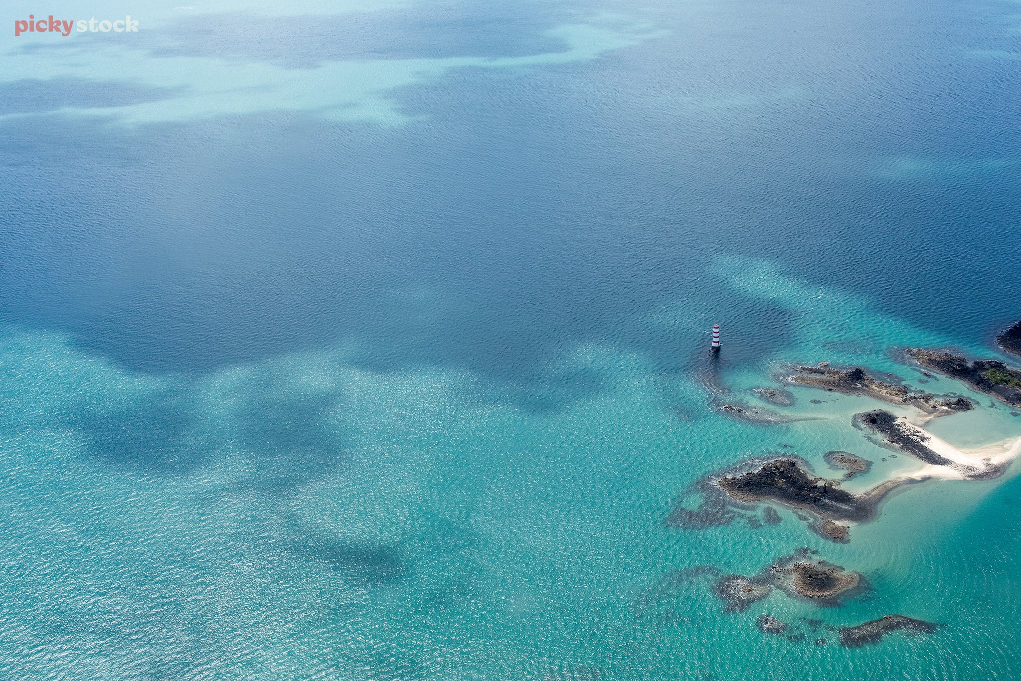 Landscape of a high aerial shot of a sandy reef and lighthouse, the clear waters are a patchwork f different hues and depths.