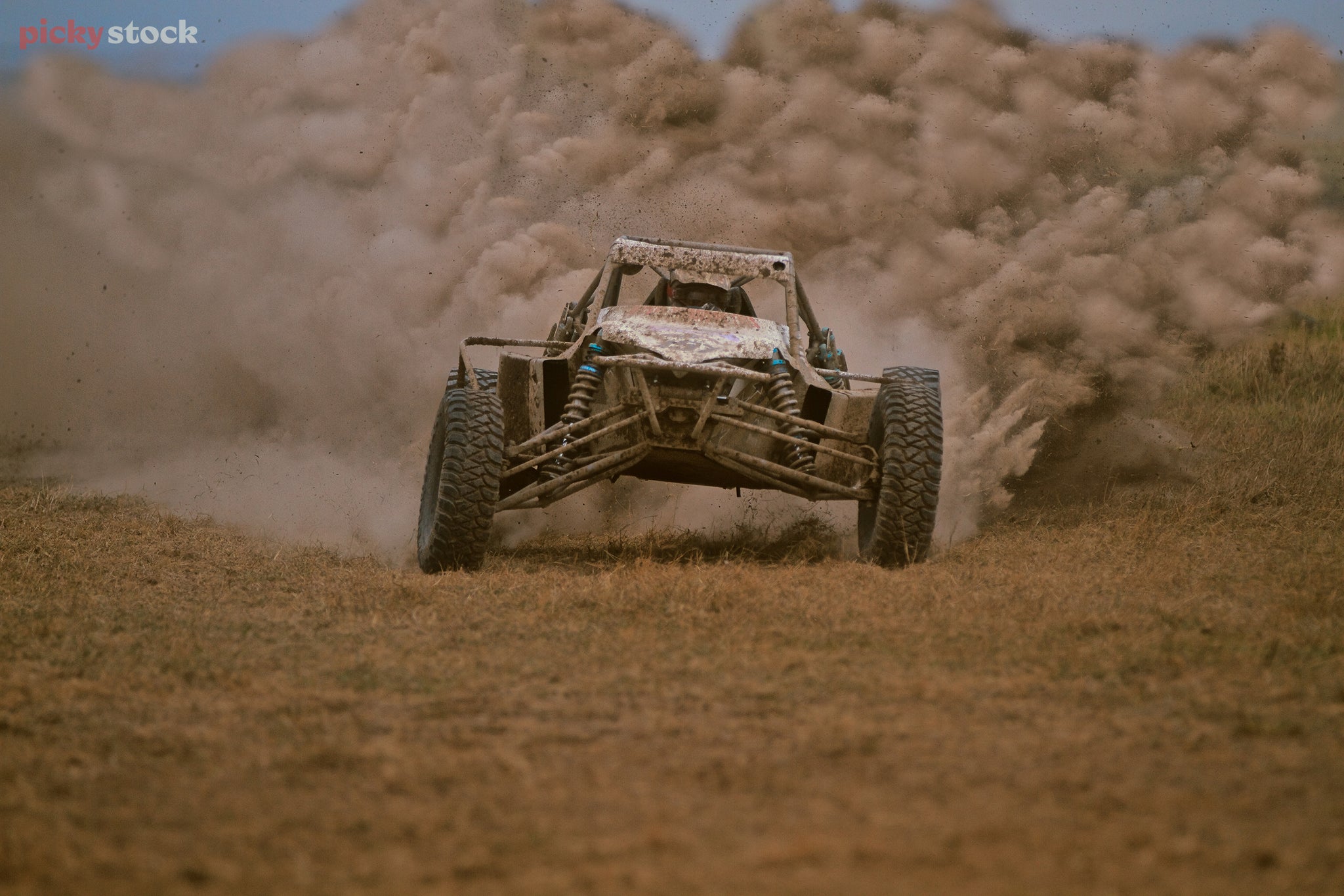 Landscape close-up of a motor sports car hurling towards the camera, caked in mud and producing large billowing plumes of dust.
