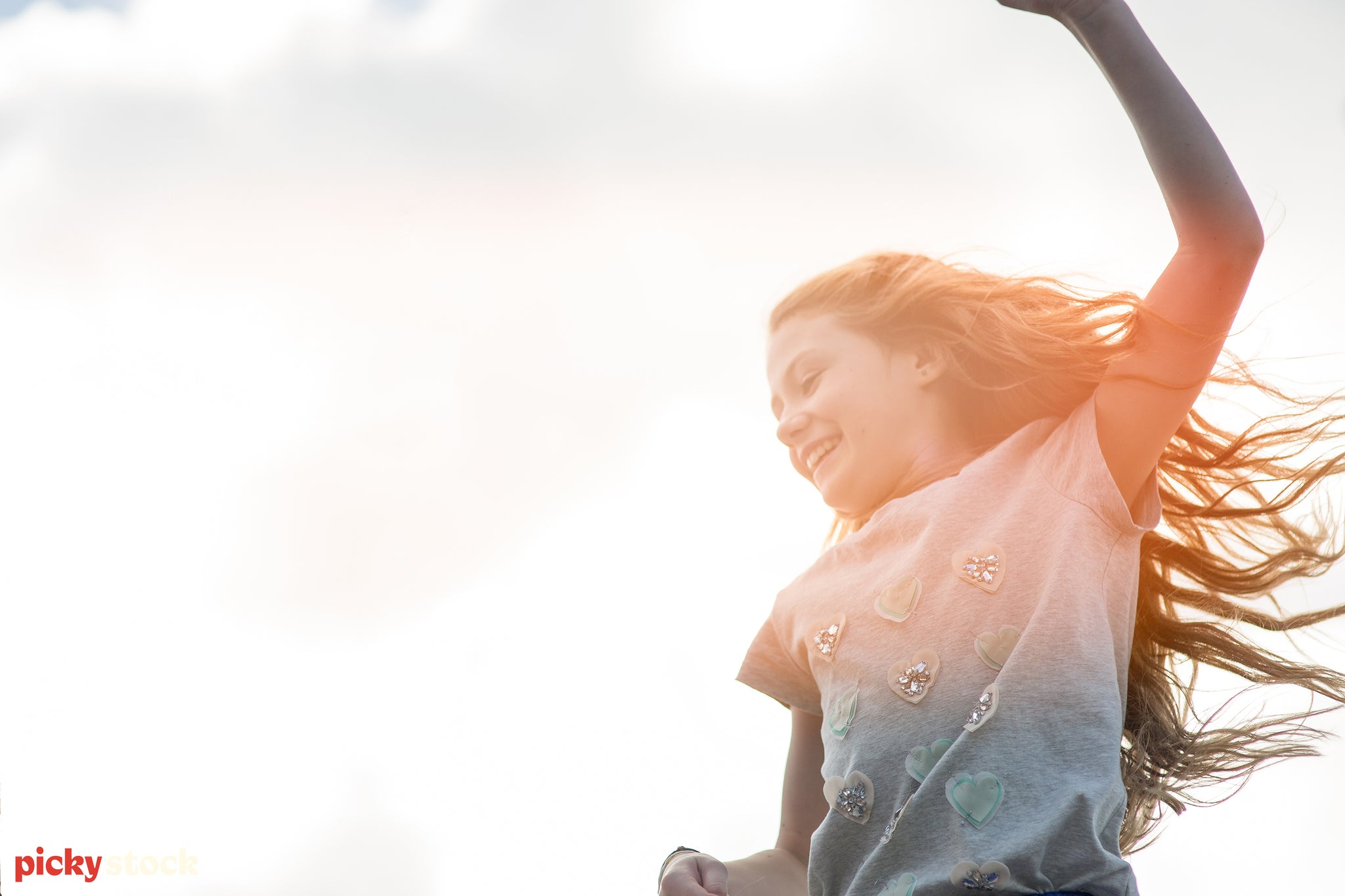 Landscape close-up of a young girl running while the sun shines an orange veil over her face while the wind blows her hair.